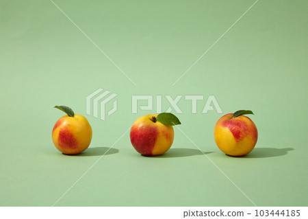 Front view of three colorful peaches (prunus persica) still green petioles arranged on a light green background. Peaches are very nutritious and can provide many health benefits 103444185