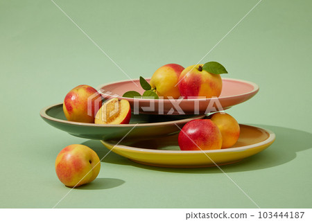 Front view of fresh peaches (prunus persica) decorated on a light background with round colorful plates. Creative background for advertising.  103444187