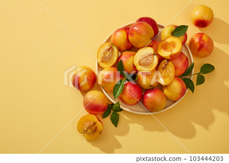 Colorful fresh ripe peaches (prunus persica) with green leaves on the stem are placed on a round plate and decorated on a yellow background. Minimal scene with copy space Colorful fresh ripe peaches (prunus persica) with green leaves on the stem are placed on a round plate and decorated on a yellow background. Minimal scene with copy space 103444203