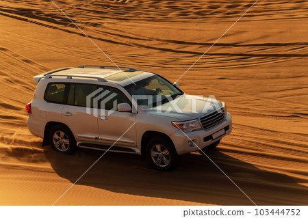White car driving in Rub al Khali Desert at the Empty Quarter, in Abu Dhabi, United Arab Emirates at sunset 103444752