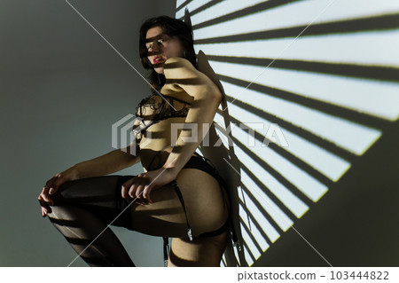 Black and white photo of a beautiful young woman in lace lingerie with a shadow pattern on the face and body in the form of stripes 103444822