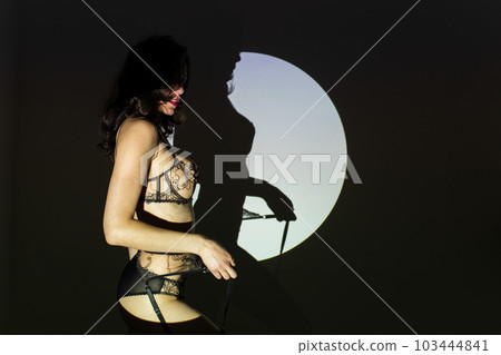 Black and white photo of a beautiful young woman in lace lingerie with a shadow pattern on the face and body in the form of circle 103444841