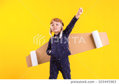 Freedom, girl playing to be airplane pilot, funny little girl with aviator cap and glasses, carries wings made of brown cardboard as an airplane Freedom, girl playing to be airplane pilot, funny little girl with aviator cap and glasses, carries wings made of brown cardboard as an airplane 103445963