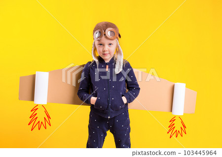 Freedom, girl playing to be airplane pilot, funny little girl with aviator cap and glasses, carries wings made of brown cardboard as an airplane 103445964