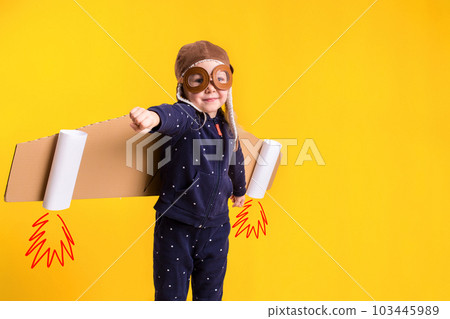 Freedom, girl playing to be airplane pilot, funny little girl with aviator cap and glasses, carries wings made of brown cardboard as an airplane Freedom, girl playing to be airplane pilot, funny little girl with aviator cap and glasses, carries wings made of brown cardboard as an airplane 103445989