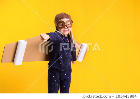 Freedom, girl playing to be airplane pilot, funny little girl with aviator cap and glasses, carries wings made of brown cardboard as an airplane 103445994