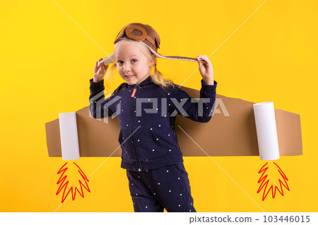 Freedom, girl playing to be airplane pilot, funny little girl with aviator cap and glasses, carries wings made of brown cardboard as an airplane Freedom, girl playing to be airplane pilot, funny little girl with aviator cap and glasses, carries wings made of brown cardboard as an airplane 103446015
