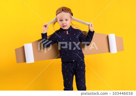 A little child girl is wearing homemade cardboard flying wings, pretending to be a pilot for a craft, imagination or exploration concept. 103446038