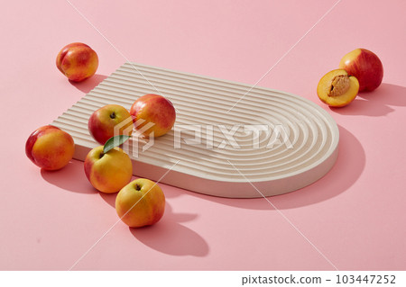 Fresh fruit concept with several small peaches placed on the podium over a pink background. Thanks to vitamins A and C, Peach (Prunus persica) helps improve health 103447252