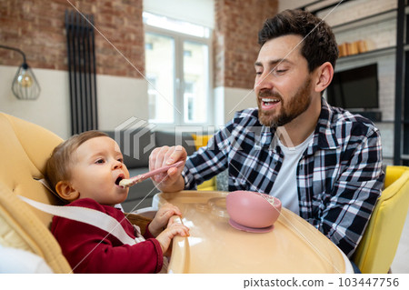 Father teaching his little baby to eat porridge from spoon infant daughter. Father teaching his little baby to eat porridge from spoon infant daughter. 103447756