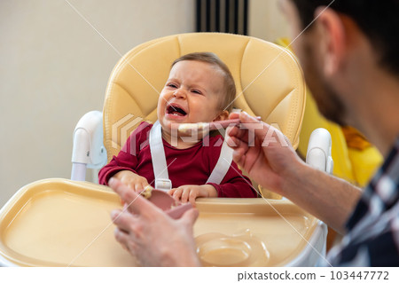 Father feeding crying toddler daughter holding spoon kid eating puree. Father feeding crying toddler daughter holding spoon kid eating puree. 103447772