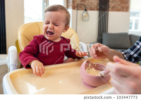 Infant little baby girl crying and don't want to eat food from her father. Infant little baby girl crying and don't want to eat food from her father. 103447773