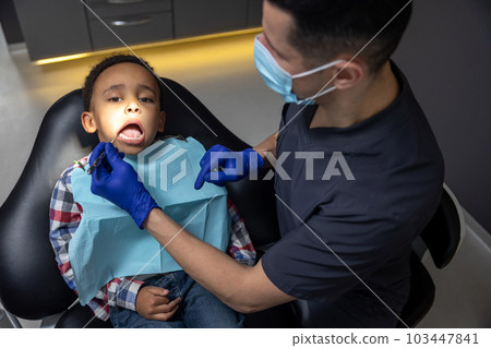 Dark-skinned boy looking scared while doctor checking his teeth 103447841