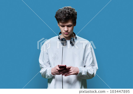 Young serious male with headphones using smartphone, on blue background 103447895