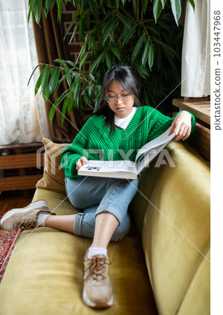 Young asian girl with a big book sitting on the sofa 103447968
