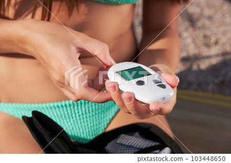 A diabetic patient checks and measures his blood glucose level with a glucometer on the beach. 103448650