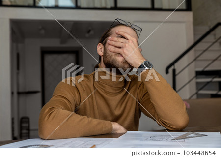 Exhausted tired engineer architect working on design of house, creating blueprint, being overworked. 103448654