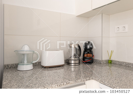 Close-up of a kitchen table with a juicer and kitchen appliances with white tiles and kitchen cabinets. The concept of household utensils and convenient gadgets for cooking 103450527