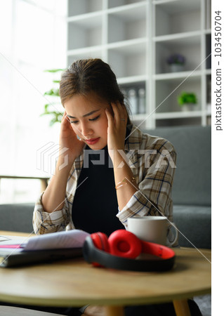 Stressed young woman holding head in hands, managing household finances frustrated with family financial problems Stressed young woman holding head in hands, managing household finances frustrated with family financial problems 103450704