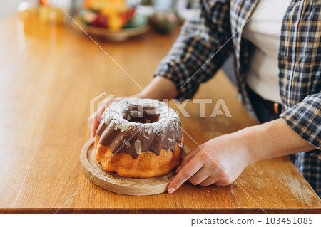 Close up of woman hand with round chocolate almond cake on wooden desk in the kitchen. Culinary, baking and cooking food concept Close up of woman hand with round chocolate almond cake on wooden desk in the kitchen. Culinary, baking and cooking food concept 103451085