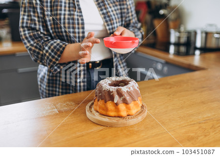 Happy redhead Woman making homemade cake with easy recipe, sprinkling powdered sugar on top. Icing sugar sprinkled with colander. Culinary, baking and cooking food concept Happy redhead Woman making homemade cake with easy recipe, sprinkling powdered sugar on top. Icing sugar sprinkled with colander. Culinary, baking and cooking food concept 103451087