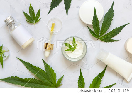 Cosmetic bottles, jars and tubes with blank label near green cannabis leaves. Mockup Cosmetic bottles, jars and tubes with blank label near green cannabis leaves. Mockup 103451119