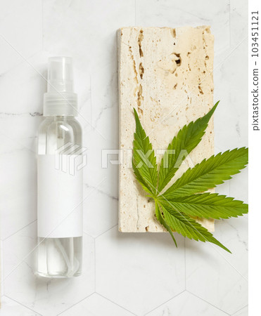 Cosmetic Bottle with blank label near green cannabis leaves and beige stones top view. Mockup Cosmetic Bottle with blank label near green cannabis leaves and beige stones top view. Mockup 103451121