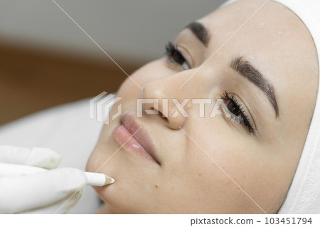 Flawless skin where botulinum therapy creates a flawless surface of the skin of the face, smoothing wrinkles and giving it youth and freshness. The woman's face is close-up. Beautician makes markup 103451794