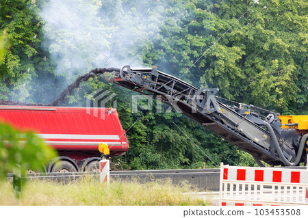 Asphalt milling and grinding machine at road repair and construction site throwing shredded old bitumen in big industrial heavy dumper tipper truck for recycling. Highway renewal with heavy machinery 103453508