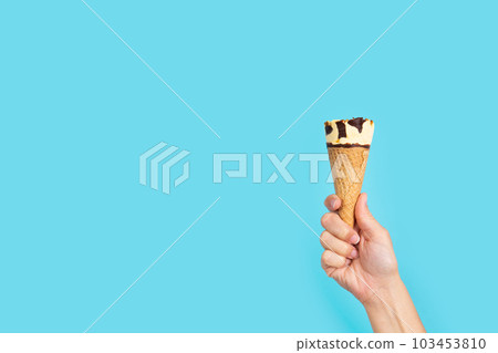 Hand holding ice cream cone on blue background Hand holding ice cream cone on blue background 103453810
