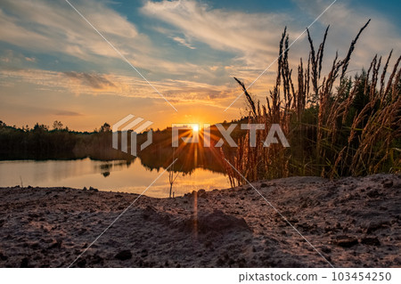 Dramatic and colorful sky at sunset or sunrise over the lake through the forest trees behind a Dramatic and colorful sky at sunset or sunrise over the lake through the forest trees behind a 103454250