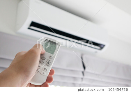 Hand with remote control directed on air conditioner 103454756