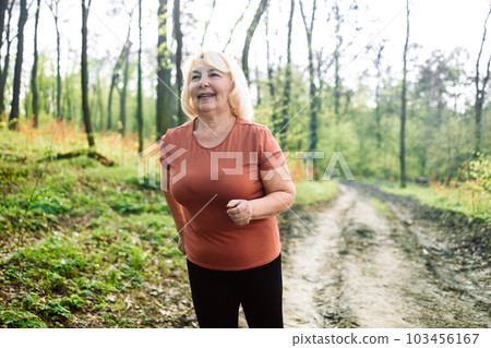 Portrait of a happy active beautiful senior caucasian woman running outdoors in nature. Active sports people. Exercise, mockup and workout with a mature female runner or athlete training outdoor in Portrait of a happy active beautiful senior caucasian woman running outdoors in nature. Active sports people. Exercise, mockup and workout with a mature female runner or athlete training outdoor in 103456167