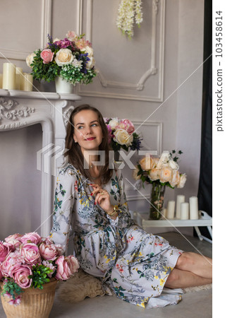 Beautiful young woman sitting in a room among the flowers Beautiful young woman sitting in a room among the flowers 103458614