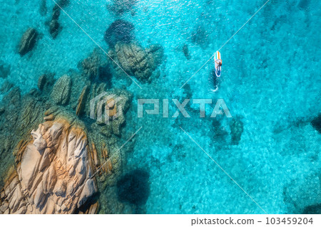 Aerial view of with man on sup board in blue sea, rocks at sunset Aerial view of with man on sup board in blue sea, rocks at sunset 103459204