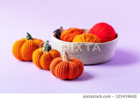 Knitted orange pumpkins in a basket on a purple background, knitting hobby, autumn composition. Halloween concept. 103459688