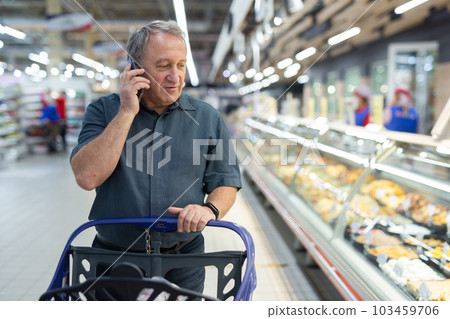 Elderly man consulting on mobile phone while shopping at grocery store 103459706