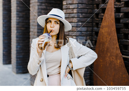 Portrait of successful business woman holding cup of cold drink in hand on her way to work on city street Portrait of successful business woman holding cup of cold drink in hand on her way to work on city street 103459735