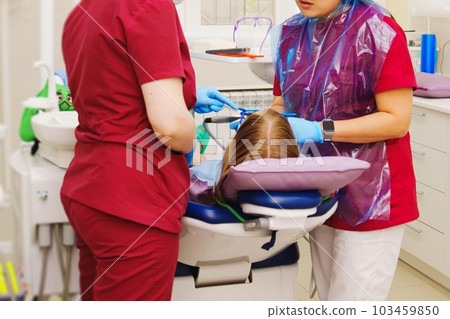A pediatric dentist treats or performs oral hygiene for a little girl. 103459850