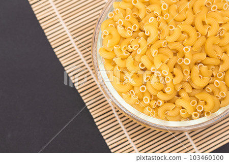 Uncooked Chifferi Rigati Pasta in Glass Jar on Bamboo Mat on Black Background Uncooked Chifferi Rigati Pasta in Glass Jar on Bamboo Mat on Black Background 103460100