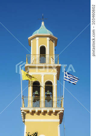 Orthodox colorful church of Saint Spiridon bell tower with Greek and Byzantine flags waving against the blue sky in Argostolion Town on the Ionian Island of Cephalonia Greece. 103460602