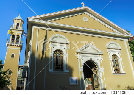 Orthodox colorful church facade of Saint Spiridon with a bell tower and Greek and Byzantine flags waving in Argostolion Town on the Ionian Island of Cephalonia Greece. 103460603
