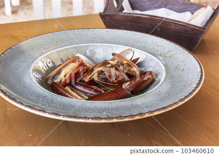 Cooked Lithofaga date shell mussels served on a dish at a wooden table. 103460610