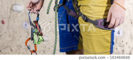 Young female climber holding carabiners for climbing, preparing for the climbing the wall in the climb center 103460698