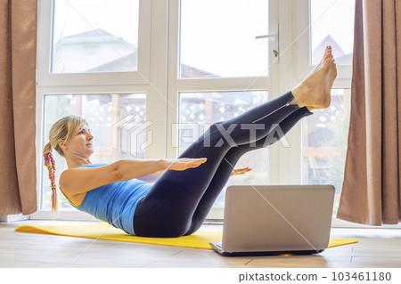 Beautiful young woman in sportswear doing sport exercises on yoga mat at home 103461180