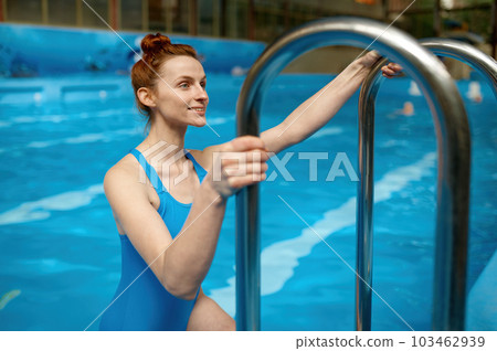Smiling young woman wearing swimsuit getting out from water in swimming pool Smiling young woman wearing swimsuit getting out from water in swimming pool 103462939