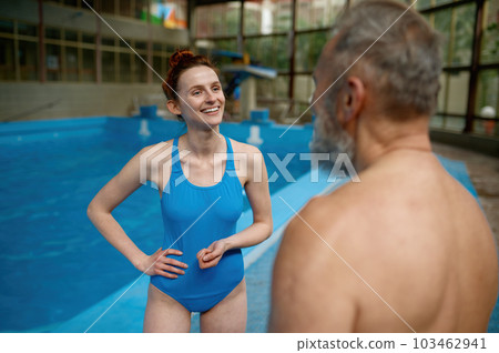 Young woman instructor talking to senior man in swimming pool 103462941