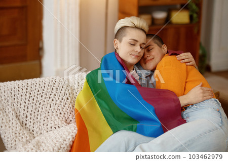 Young freedom lesbian woman cuddling in lgbt rainbow flag while sitting on sofa 103462979