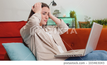 Pretty young woman use laptop surprised by bad news, fortune loss, fail, lottery results at home 103463043