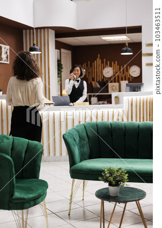 Hotel manager verifying files in lobby lounge area at reception counter, checking registration forms and booking details. Young adult ensuring to provide modern service for guests. 103463511